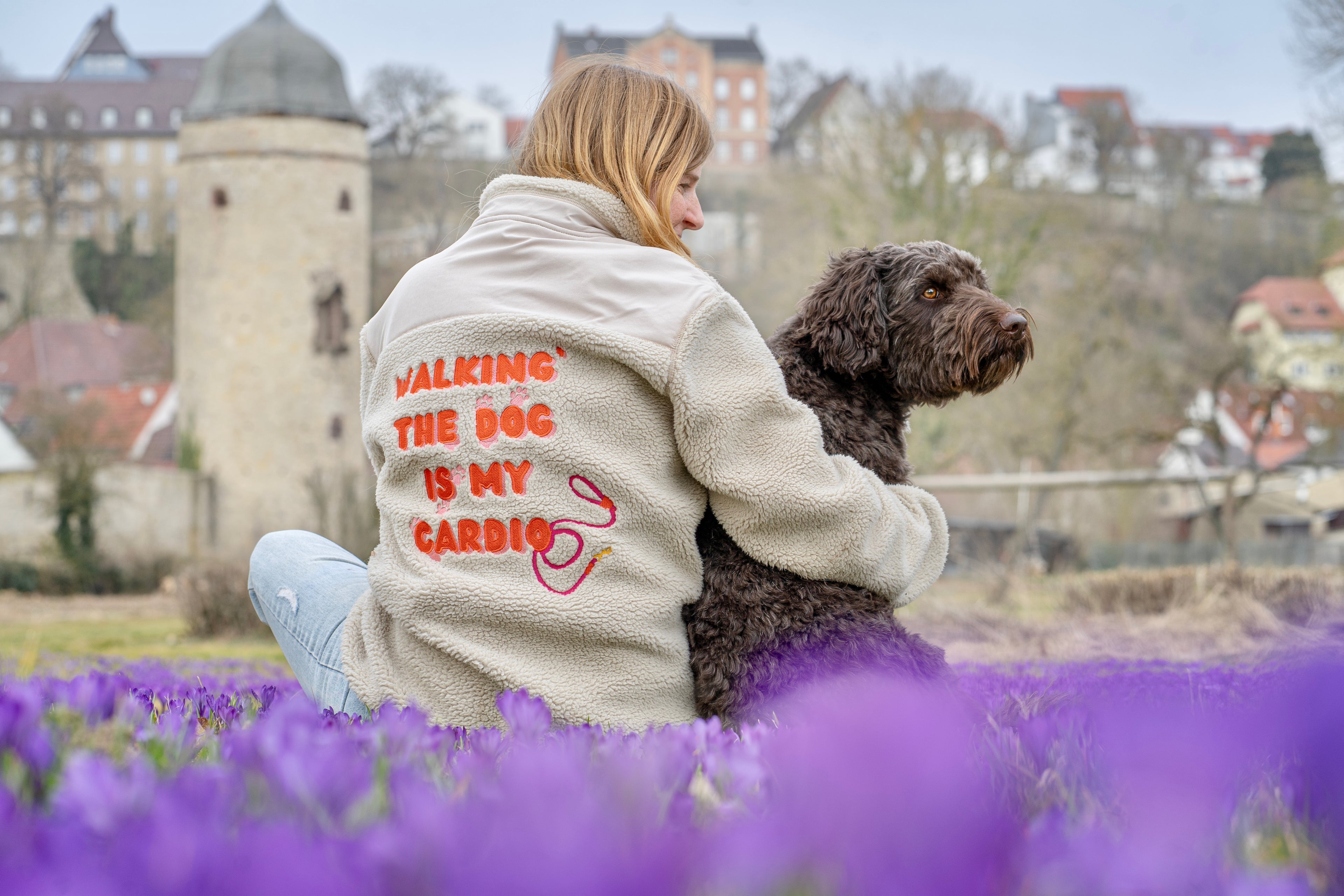 Rothaariges Mädchen spielt mit braun-weißem Labradoodle auf blühender Sommerwiese – fröhliche Hundefotografie