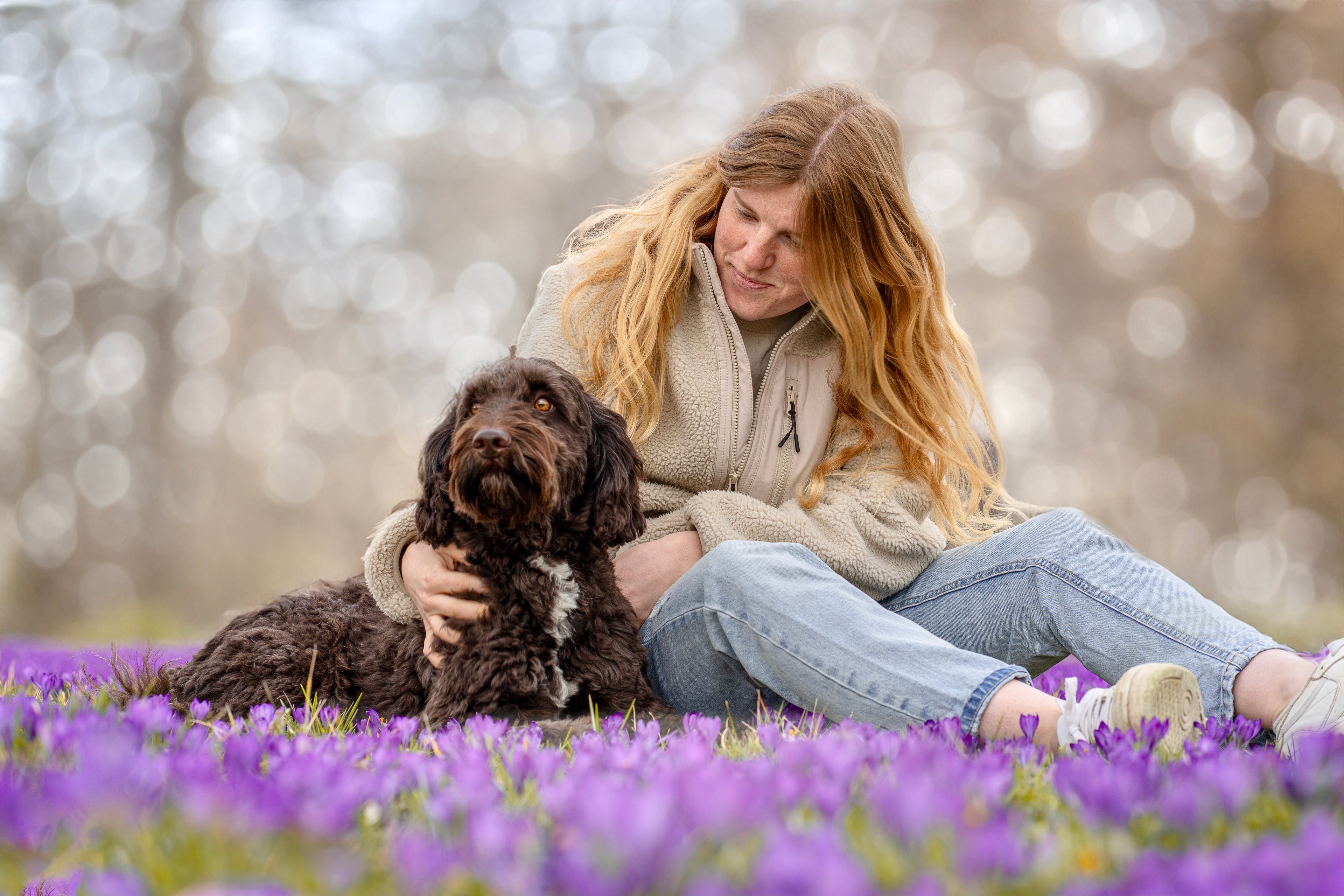 Rothaariges Mädchen spielt mit braun-weißem Labradoodle auf Sommerwiese – fröhliche Natur- und Hundefotografie